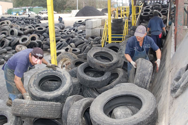 Two men collaborating on a large stack of tires, engaged in a task that requires teamwork and focus