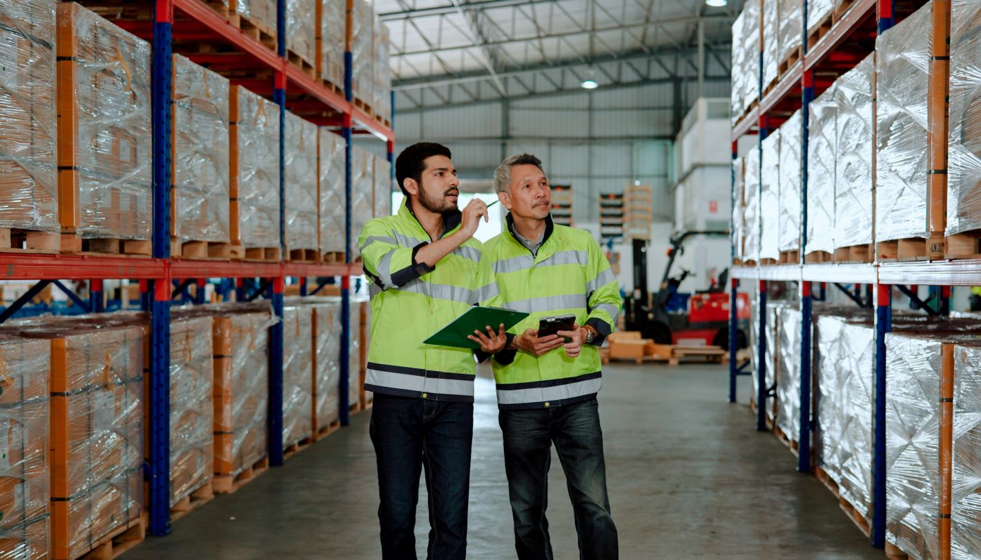 A senior warehouse worker teaching a new employee to do routine stocktaking in the company's warehouse.