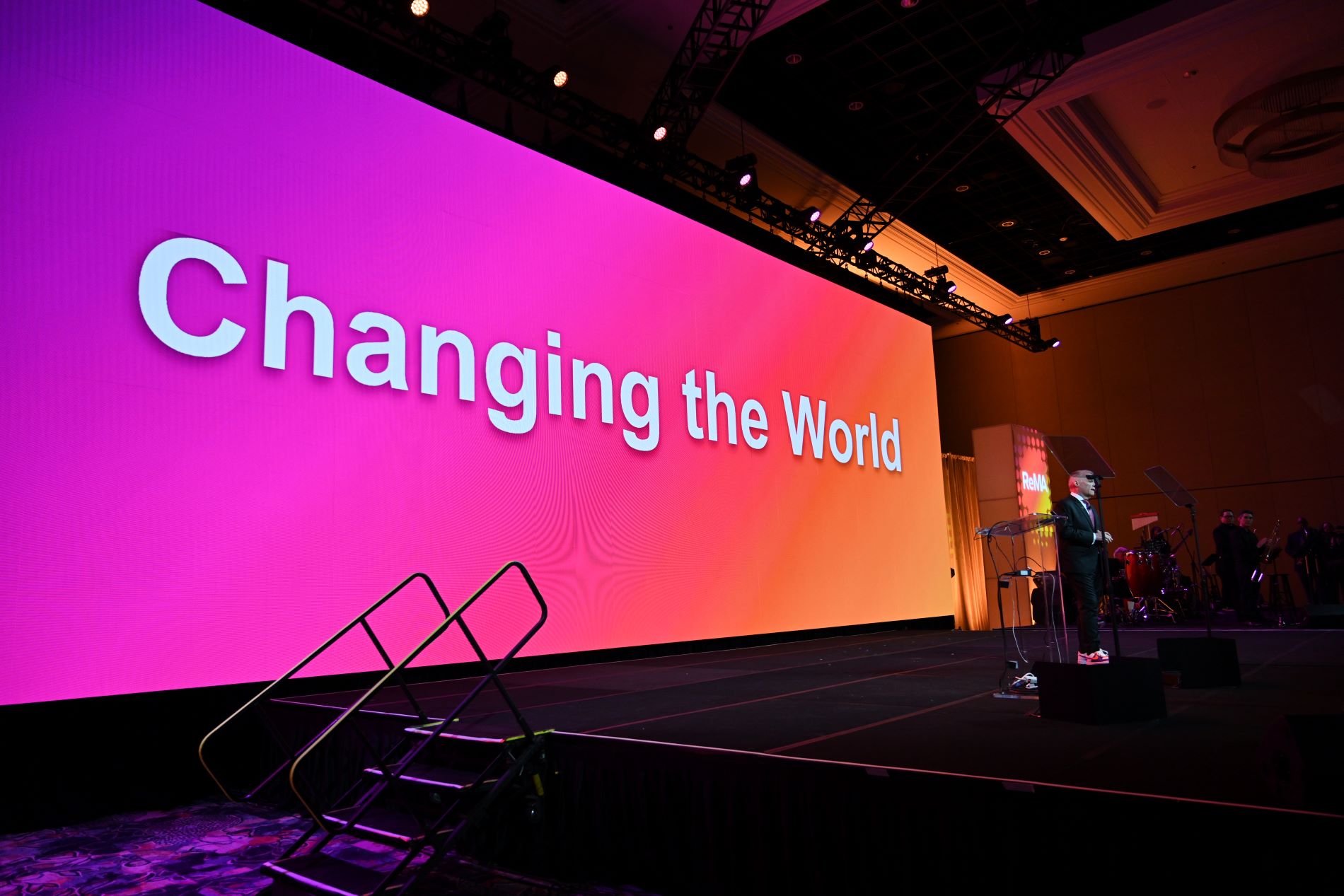 Man on stage at REMA 2024 Convention in front of multicolor screen that says Changing the World